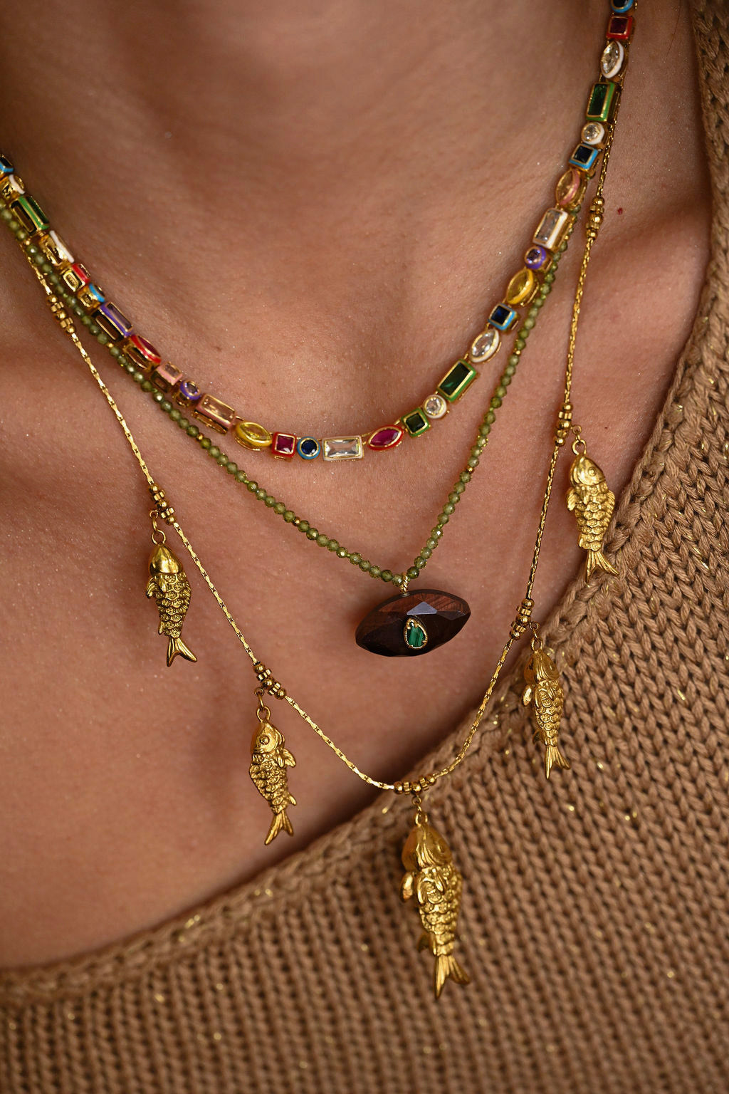 Close-up of a person wearing multiple gold necklaces with fish pendants on a brown background.