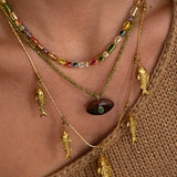 Close-up of a person wearing multiple gold necklaces with fish pendants on a brown background.