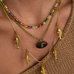 Close-up of a person wearing a gold necklace with fish charms and colorful beads.