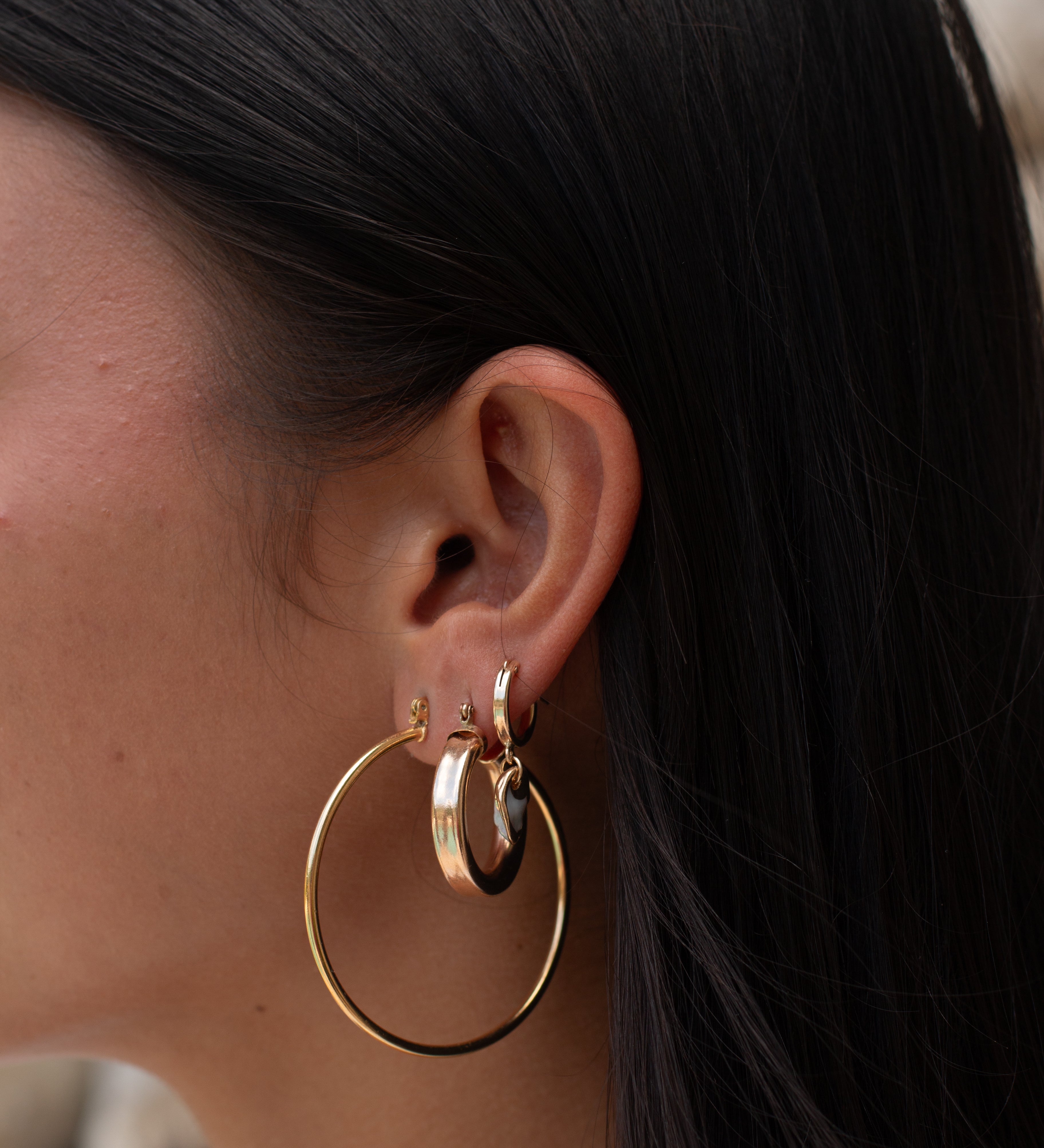 Side profile of a woman wearing three pairs of hoop earrings 