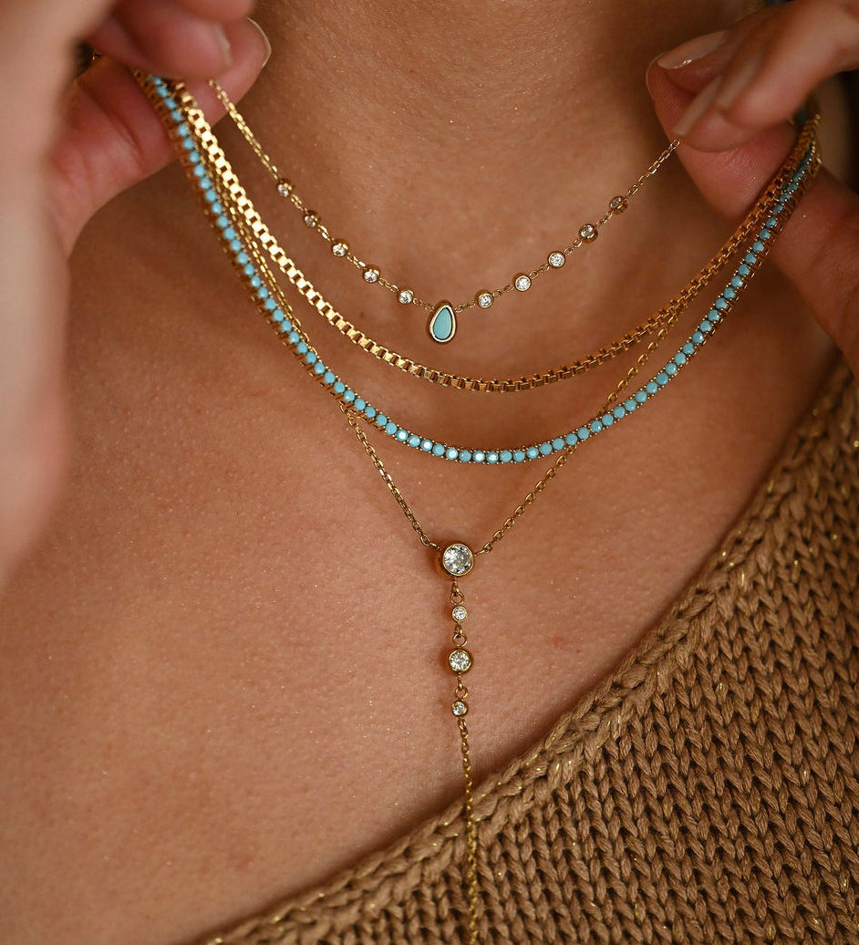 Close-up of a person wearing multiple gold and turquoise necklaces.