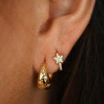 Close-up of an ear wearing gold earrings with a blurred background