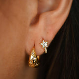 Close-up of an ear wearing gold earrings with a blurred background