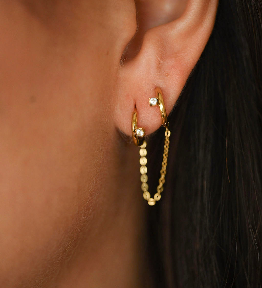 Gold hoop earrings worn by a person with dark hair.