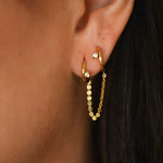 Gold hoop earrings worn by a person with dark hair.