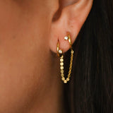Gold hoop earrings worn by a person with dark hair.