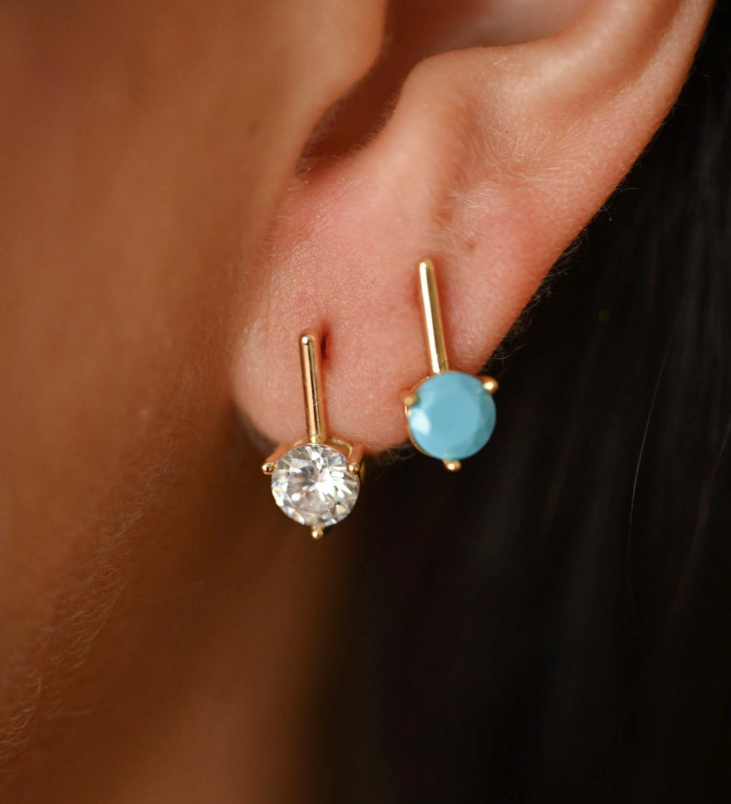 Close-up of an ear wearing two gold earrings with gemstones.