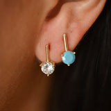 Close-up of an ear wearing two gold earrings with gemstones.