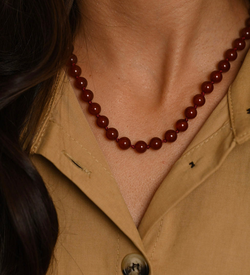 Close-up of a person wearing a brown beaded necklace and beige shirt.