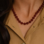 Close-up of a person wearing a brown beaded necklace and beige shirt.