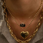 Close-up of a person wearing multiple gold necklaces with a heart pendant.