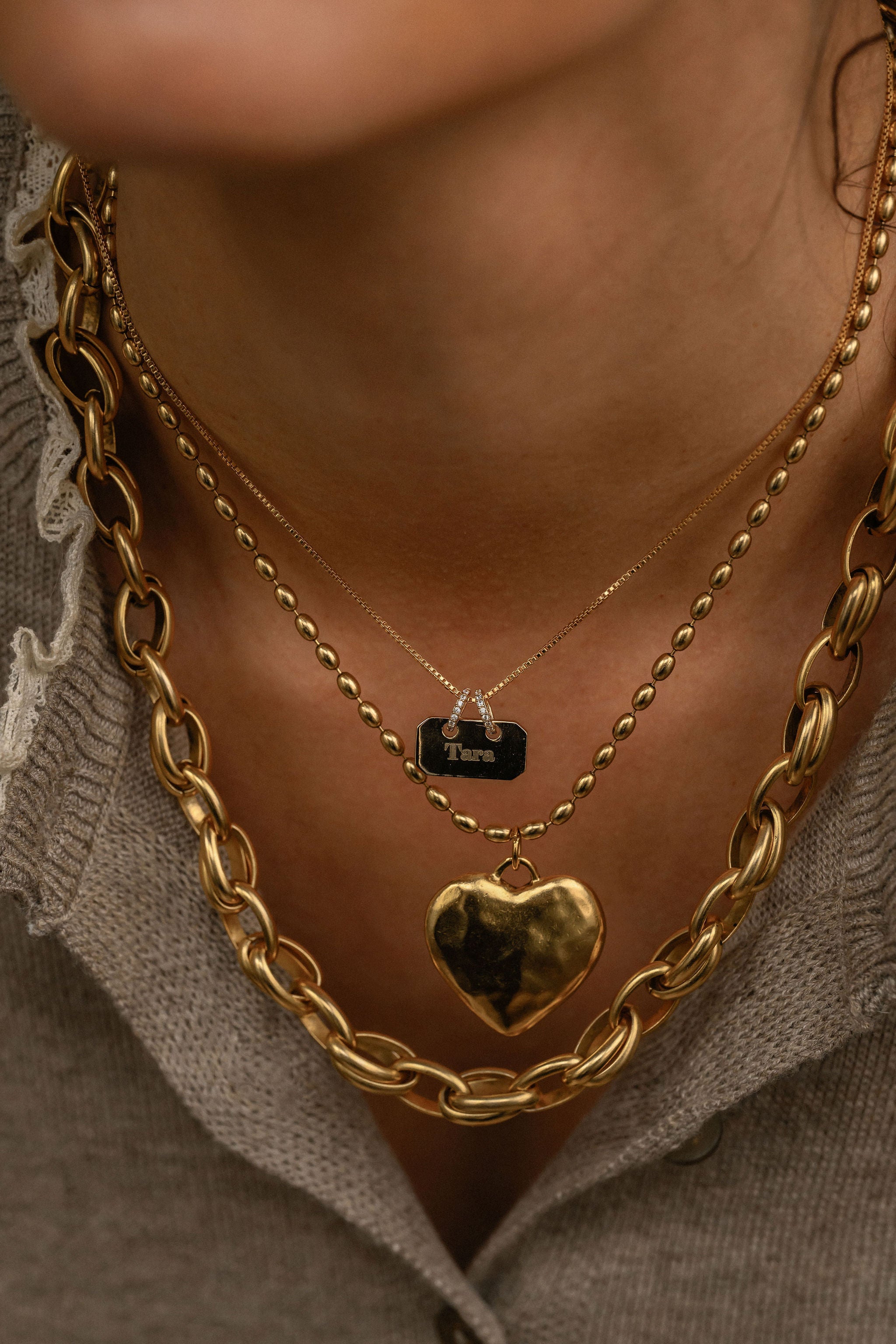 Close-up of a person wearing multiple gold necklaces with a heart pendant.