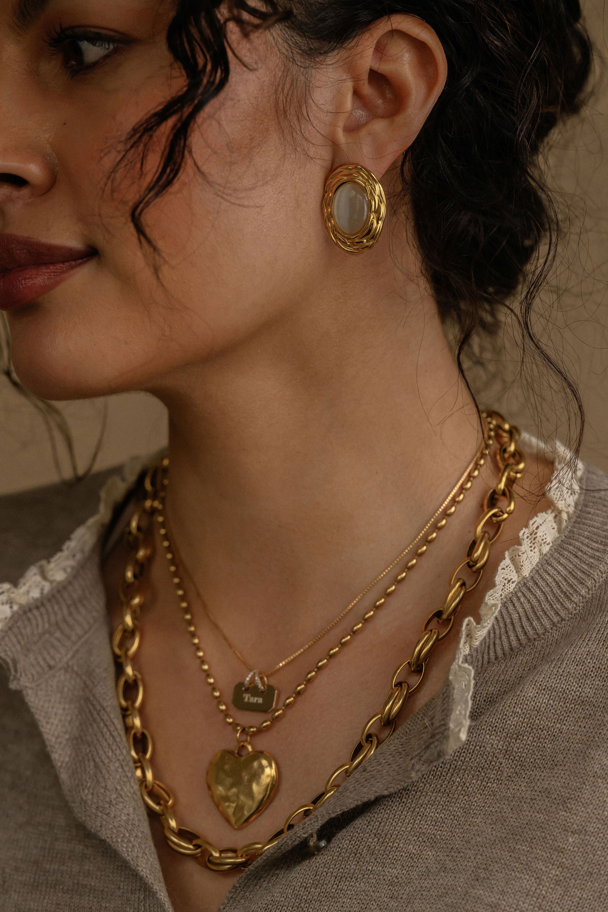 Close-up of a person wearing gold jewelry including earrings and necklaces.