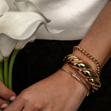 Gold bracelets on a wrist with a background of white flowers and a blurred white shirt.