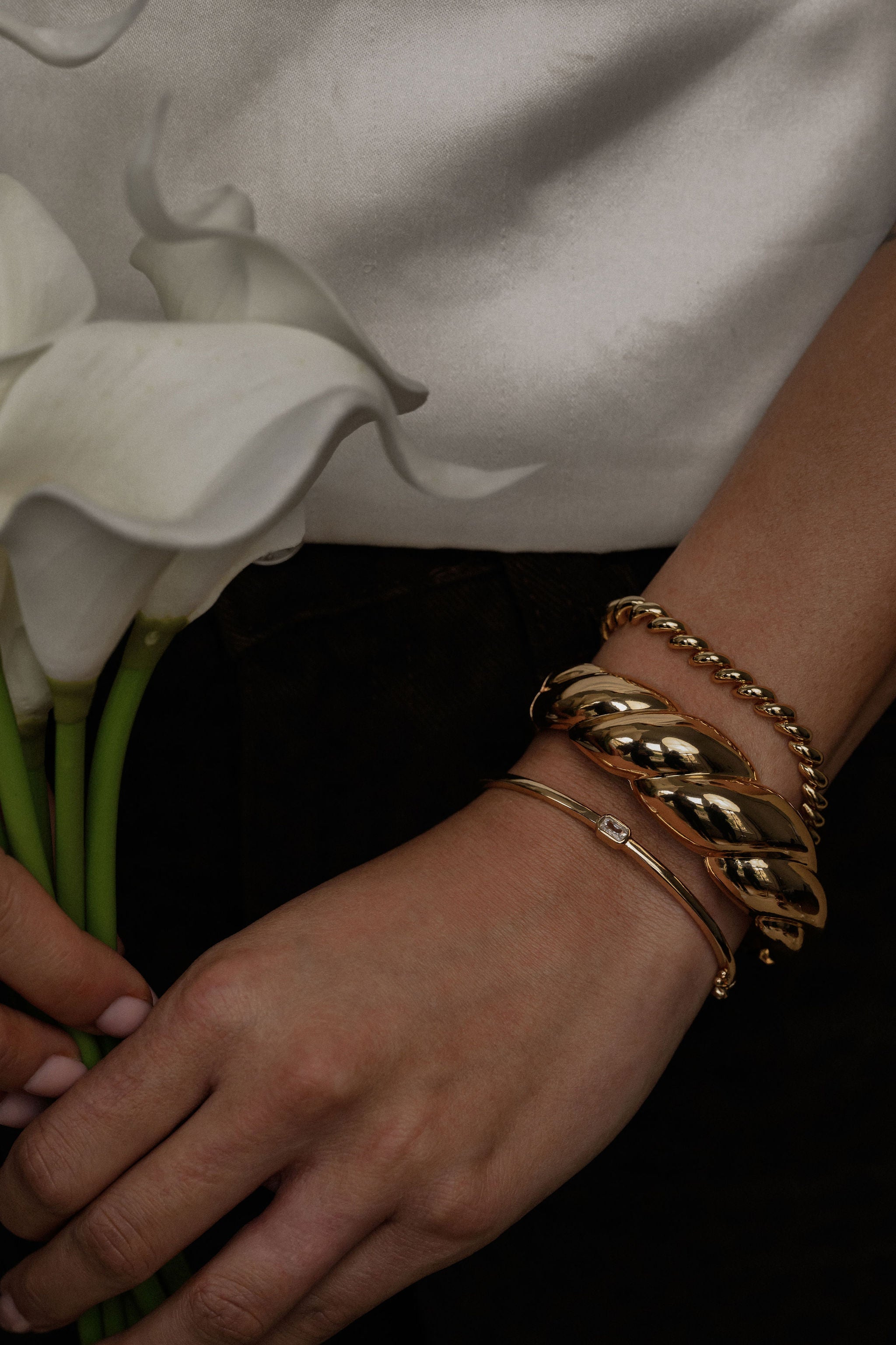 Close-up of a hand holding white flowers with gold bracelets on a dark background