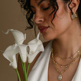 Woman holding white flowers wearing gold jewelry against a neutral background
