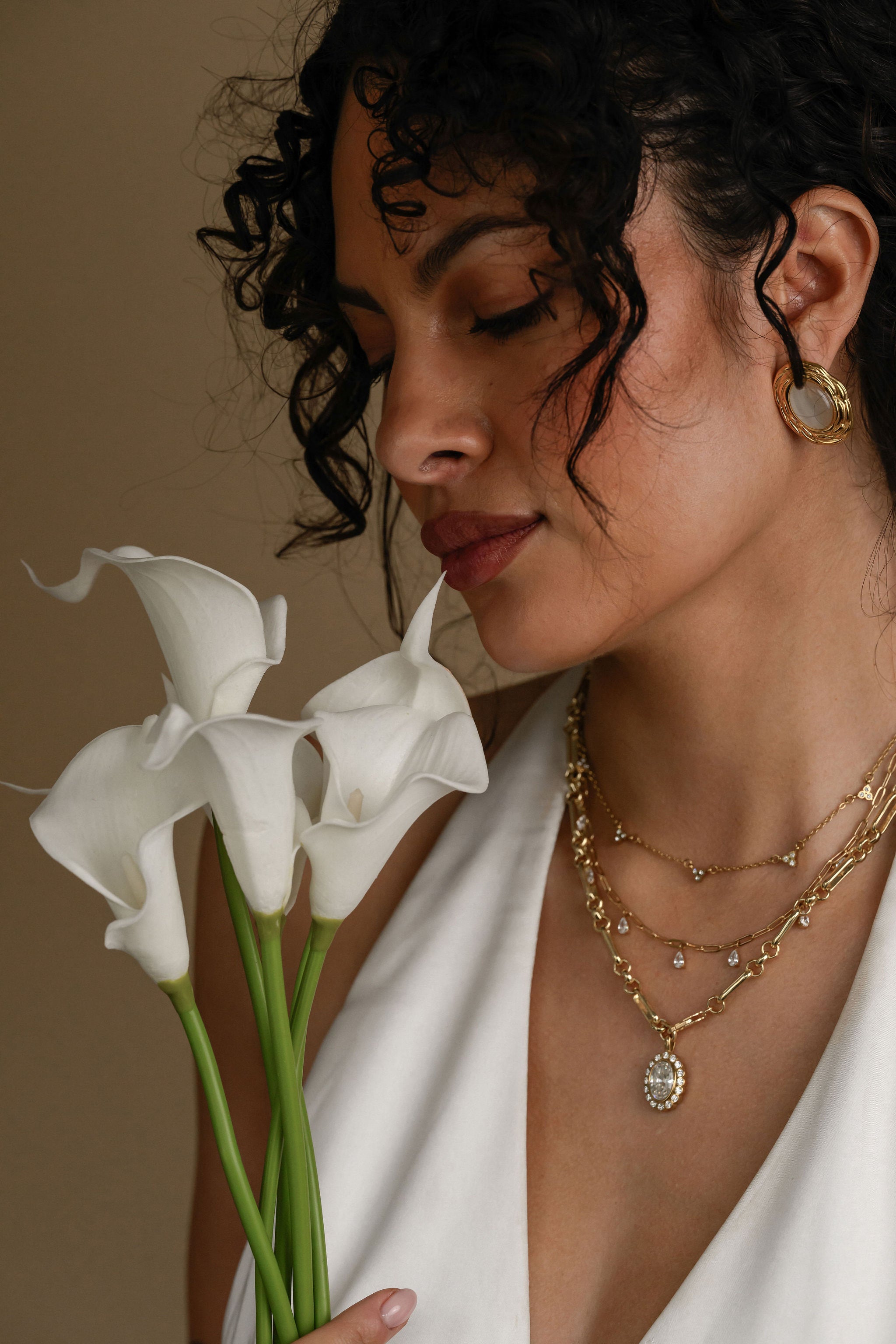 Woman holding white flowers wearing gold jewelry against a neutral background
