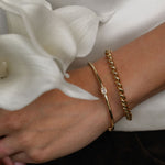 Close-up of a wrist wearing gold bracelets with white flowers in the background