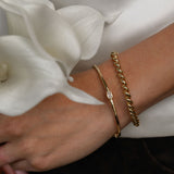 Close-up of a wrist wearing gold bracelets with white flowers in the background