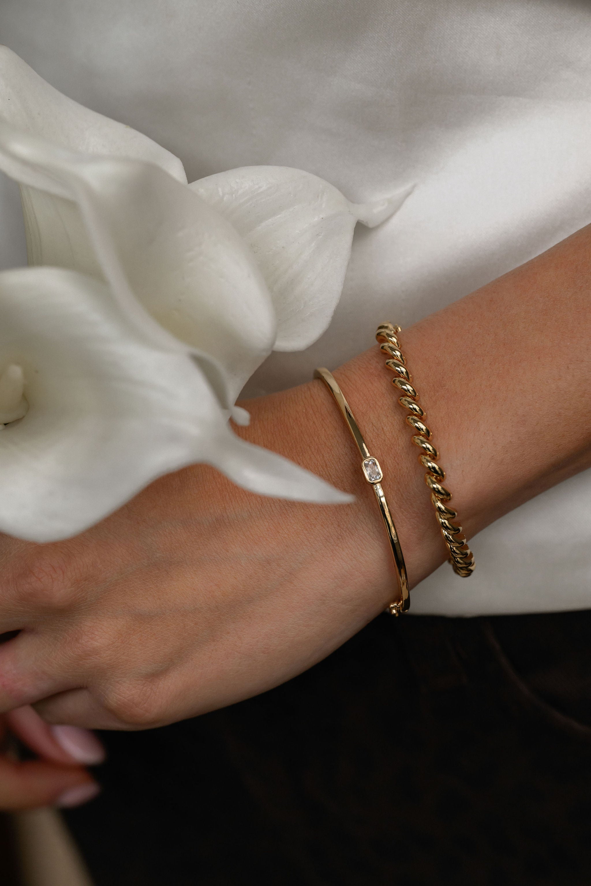 Close-up of a wrist wearing gold bracelets with white flowers in the background