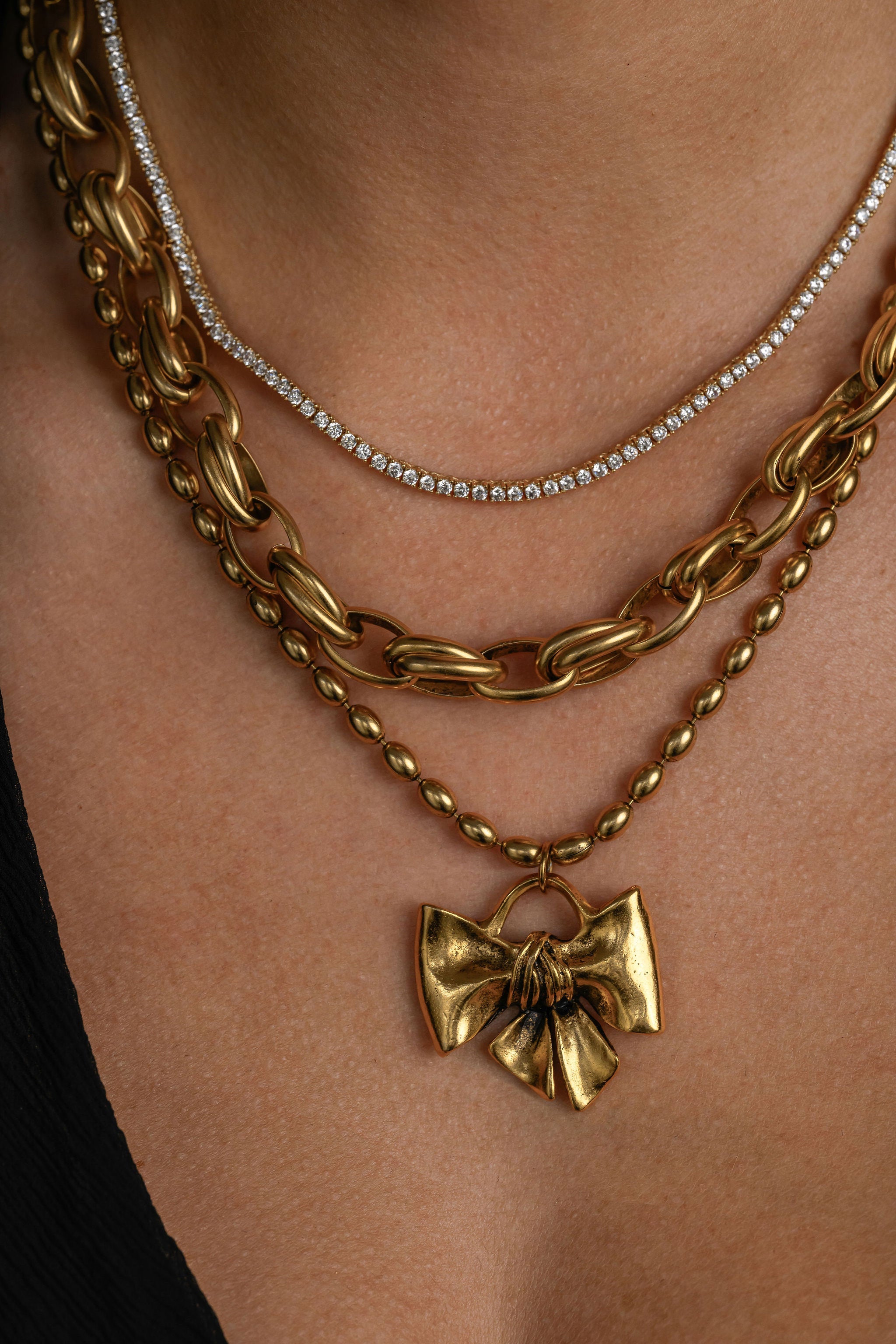 Gold chain necklace with a bow pendant on a person's neck