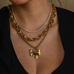 Close-up of a woman wearing multiple gold chains with a bow pendant on a neutral background