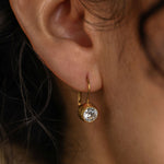Close-up of an ear wearing a gold earring with a clear gemstone.
