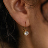 Close-up of an ear wearing a gold earring with a clear gemstone.