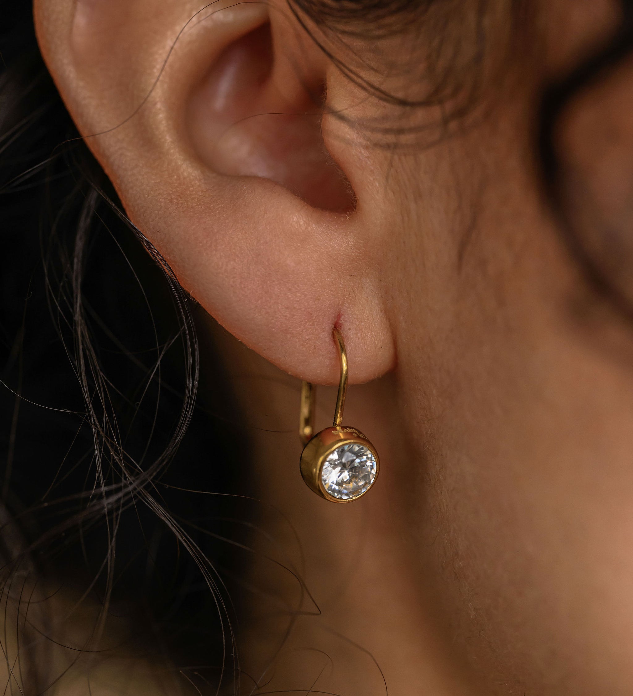 Close-up of an ear wearing a gold earring with a clear gemstone.