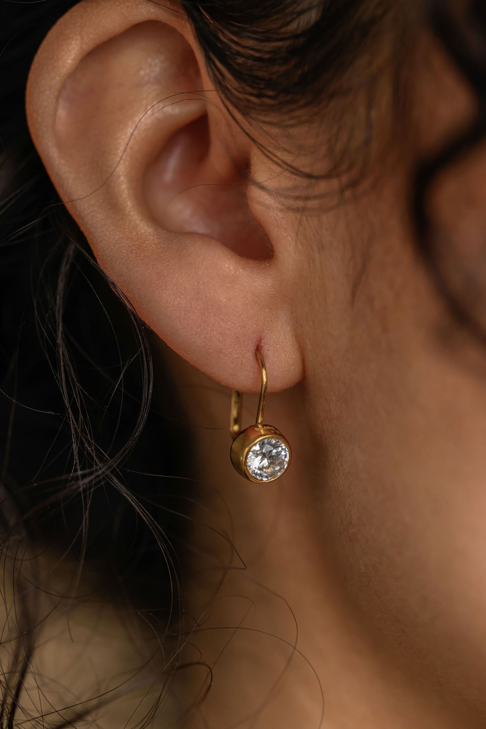 Close-up of an ear wearing a gold earring with a clear gemstone.