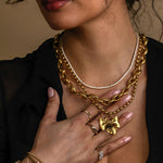 Woman wearing gold jewelry including a necklace, bracelet, and ring on a dark background