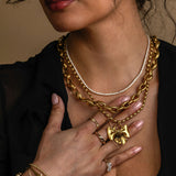 Woman wearing gold jewelry including a necklace, bracelet, and ring on a dark background