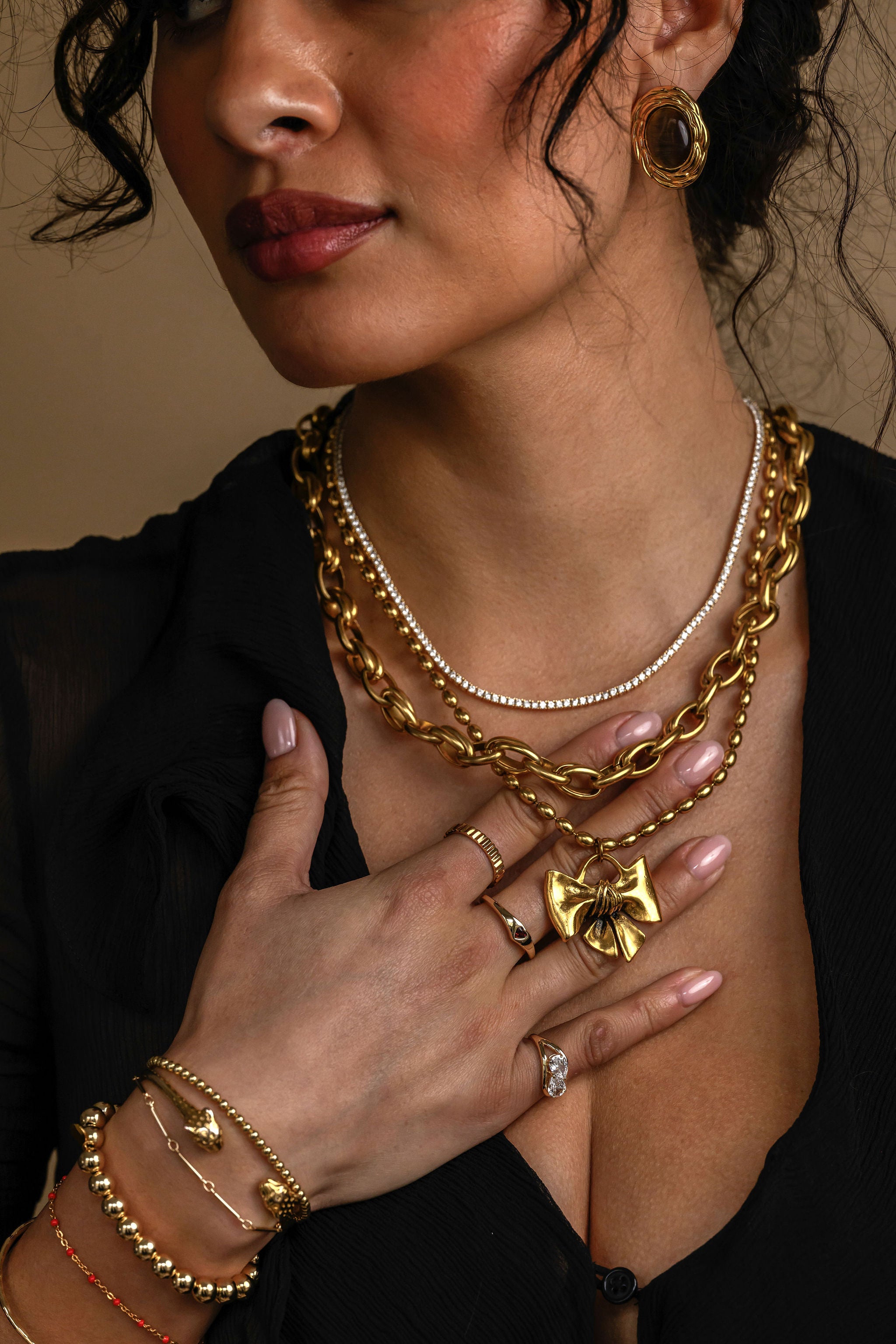 Woman wearing gold jewelry including a necklace, bracelet, and ring on a dark background