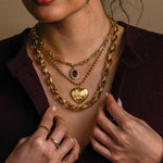 Close-up of a person wearing multiple gold necklaces and rings on a neutral background
