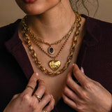 Close-up of a person wearing multiple gold necklaces and rings on a neutral background