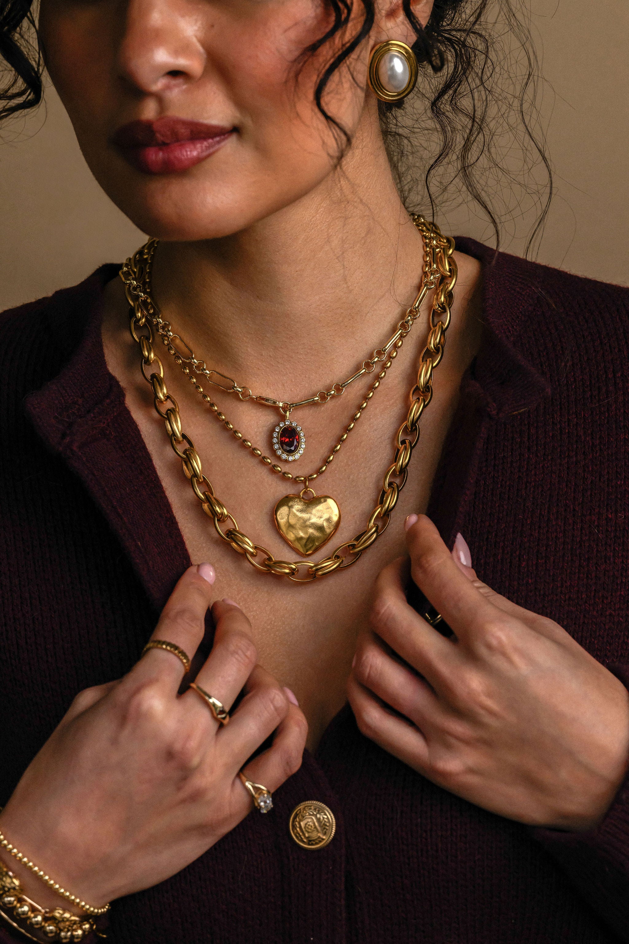 Close-up of a person wearing multiple gold necklaces and rings on a neutral background