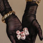 Black gloves holding white dice with red dots against a beige background