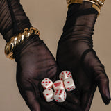 Black gloves holding white dice with red dots against a beige background
