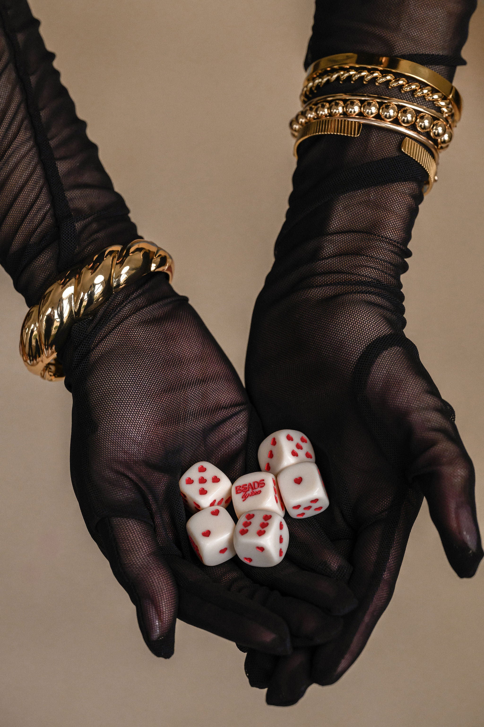 Black gloves holding white dice with red dots against a beige background