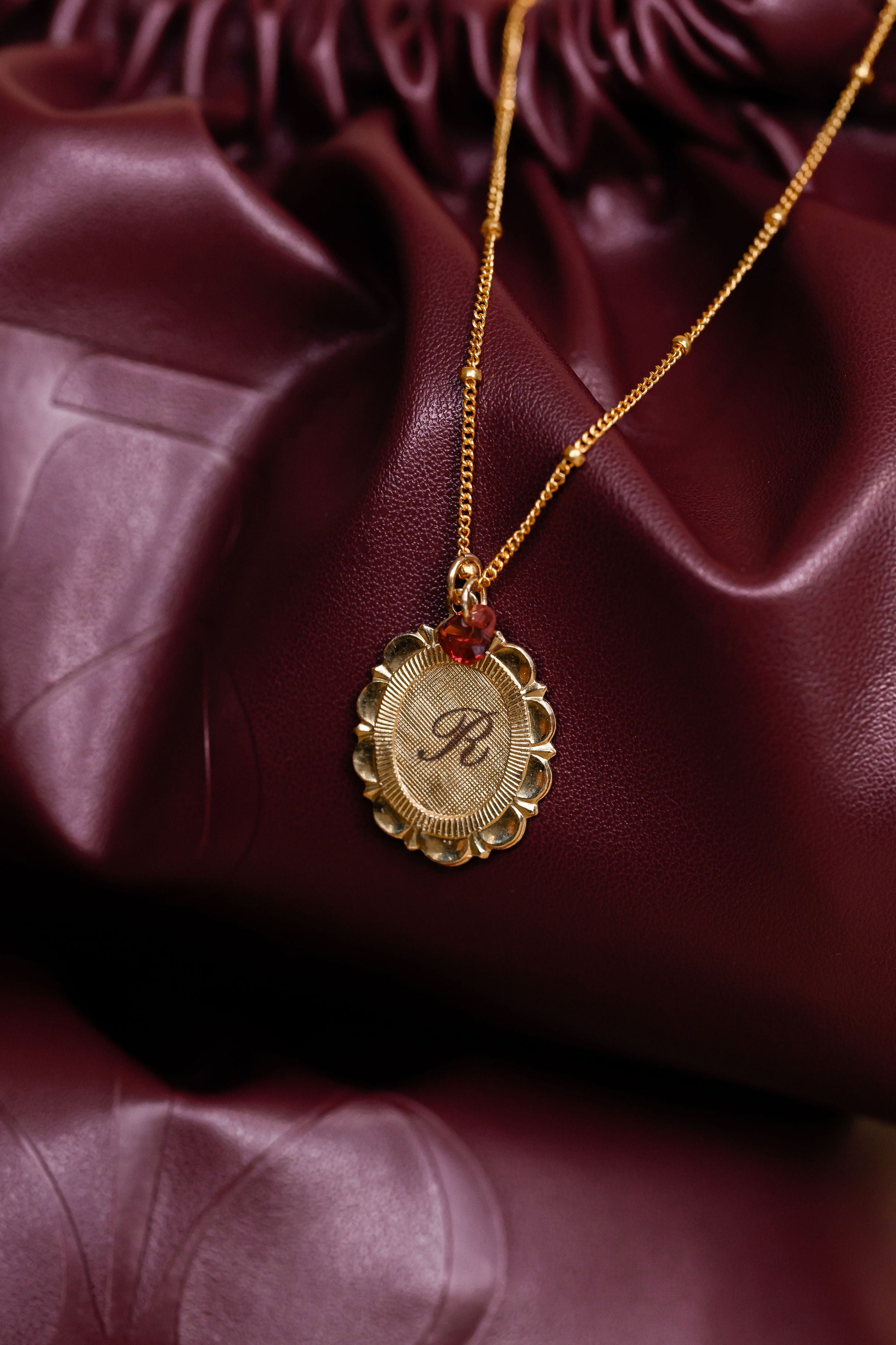 Gold necklace with a pendant on a maroon fabric background