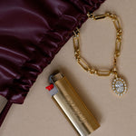 Gold lighter with chain and charm on a beige surface