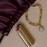Gold lighter with chain and charm on a beige surface