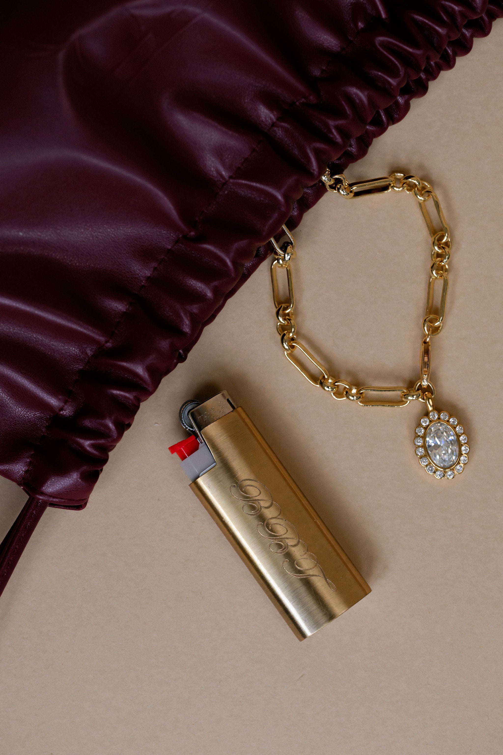 Gold lighter with chain and charm on a beige surface