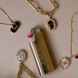 Gold necklace with pendant, lighter, and additional jewelry on a beige background
