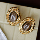 Gold earrings with brown stones on a textured surface