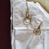 Gold earrings with clear gemstones on a textured white surface