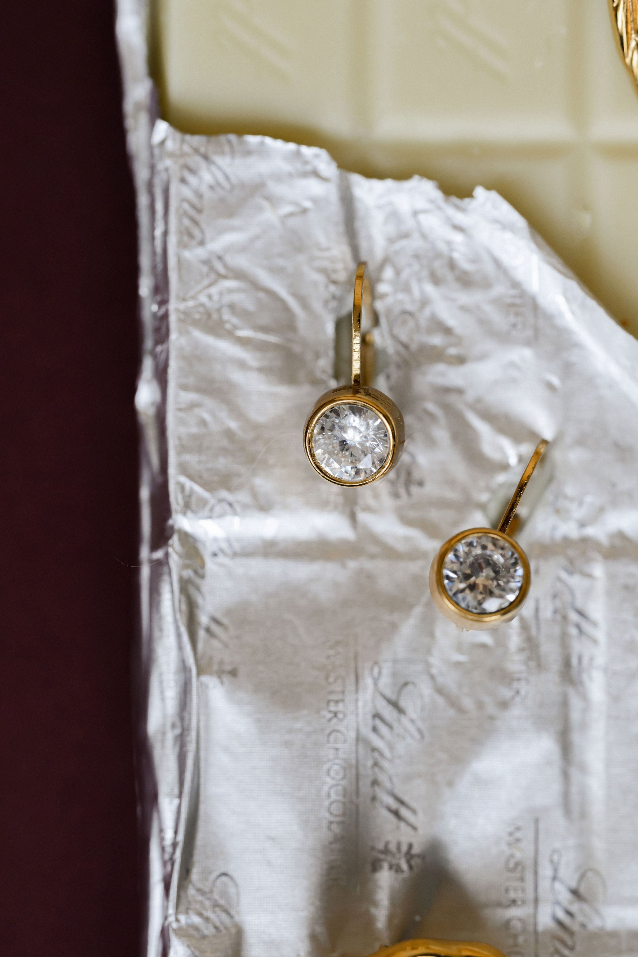 Gold earrings with clear gemstones on a textured white surface