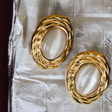 Gold hoop earrings with a central pearl-like stone on a textured paper background