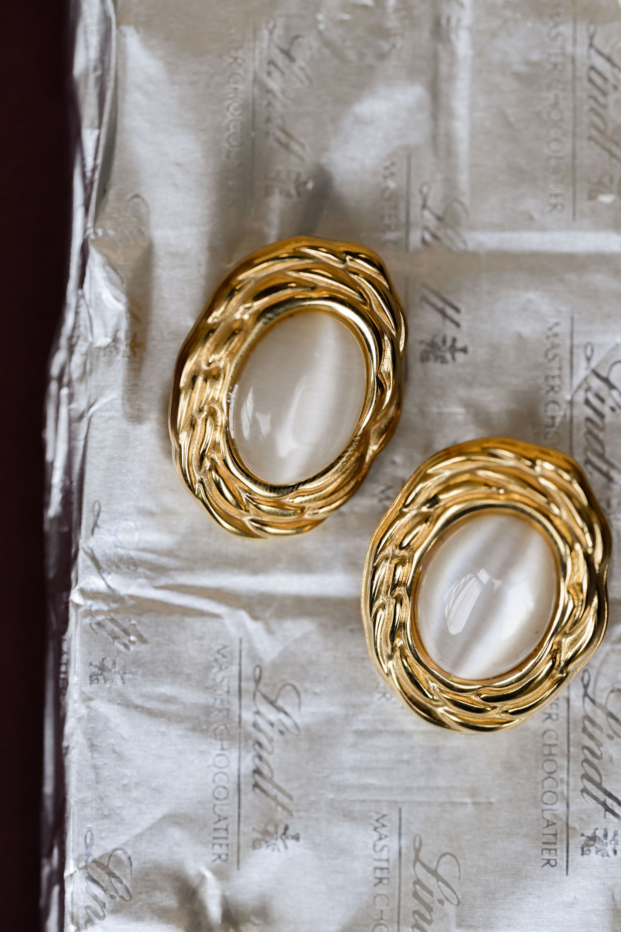 Gold hoop earrings with a central pearl-like stone on a textured paper background