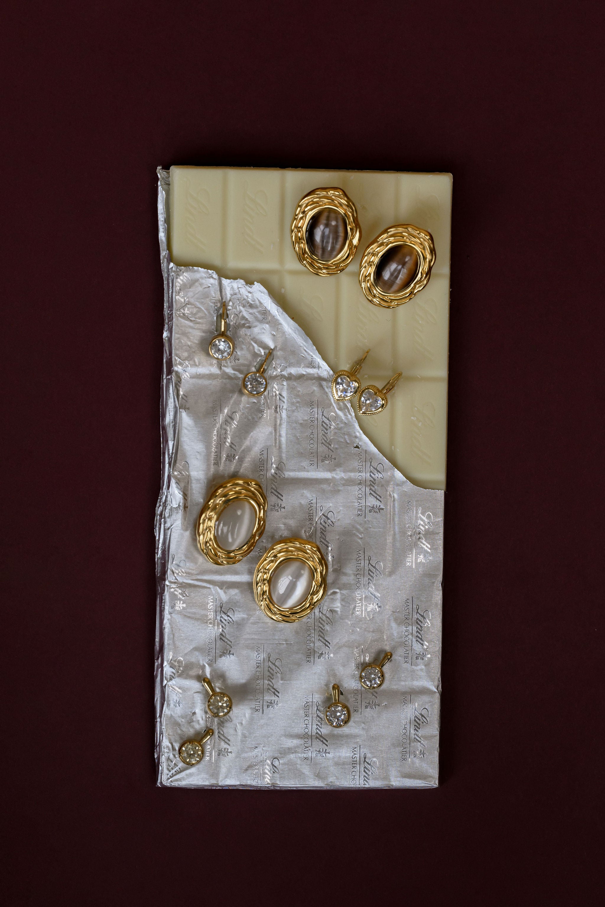 Set of gold earrings on a textured white card against a dark red background